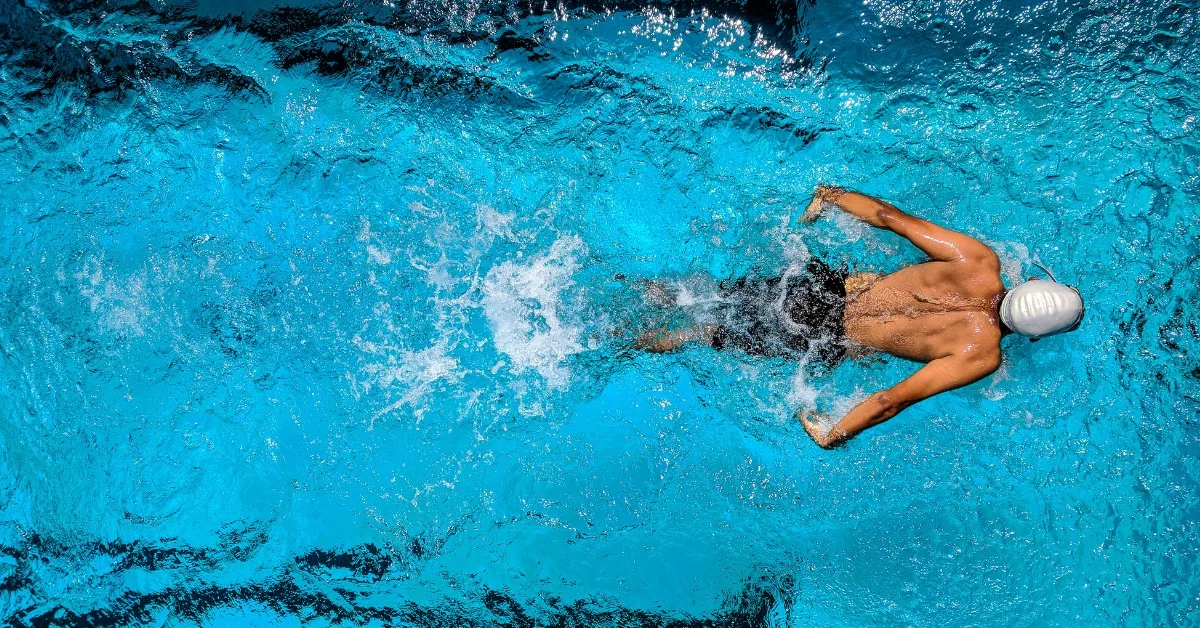Overhead photo of a man in a swimming pool, he's wearing black swimming skins and a white cap.